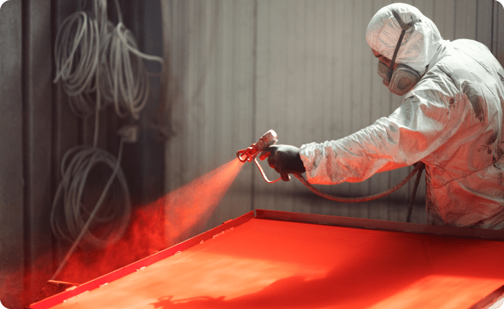A person spray painting a surface with red paint.