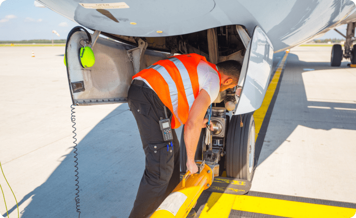 Worker in safety vest inspecting aircraft landing gear.