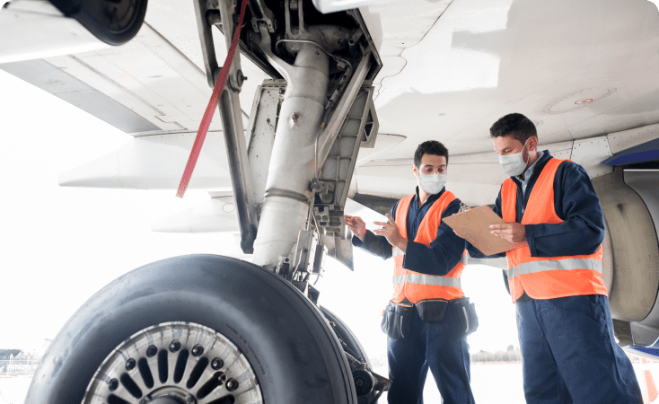 Two technicians inspecting an airplane's landing gear in a hangar.